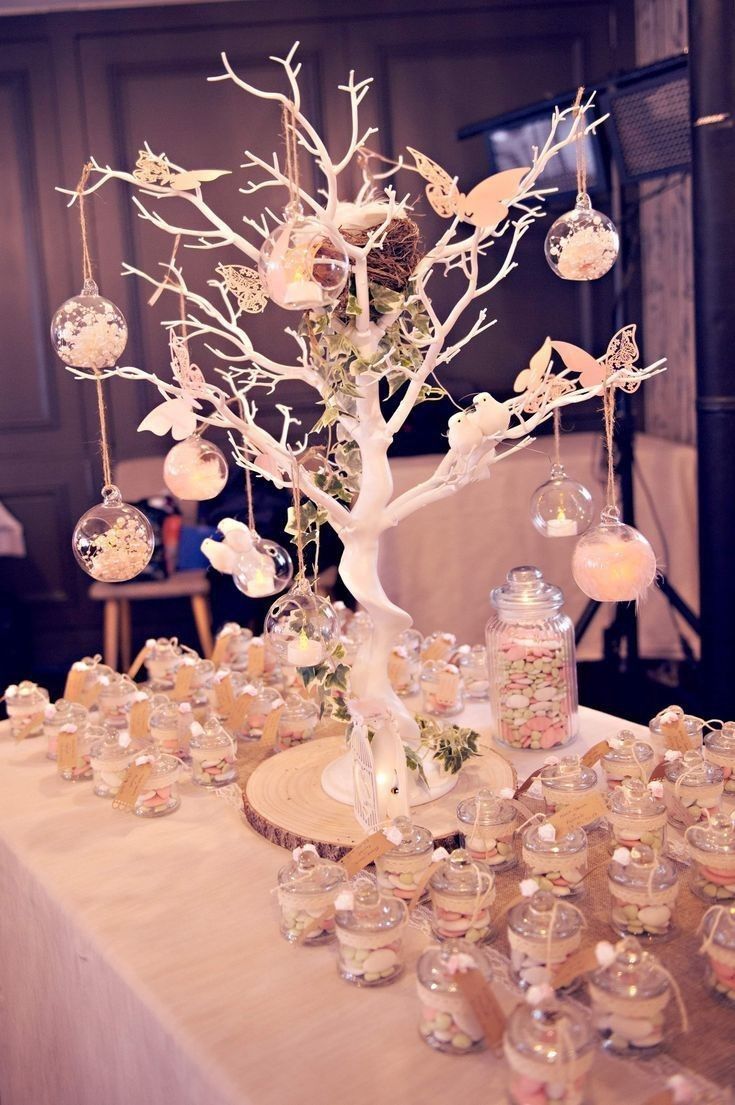 a table topped with lots of glass vases filled with flowers and candles next to a tree