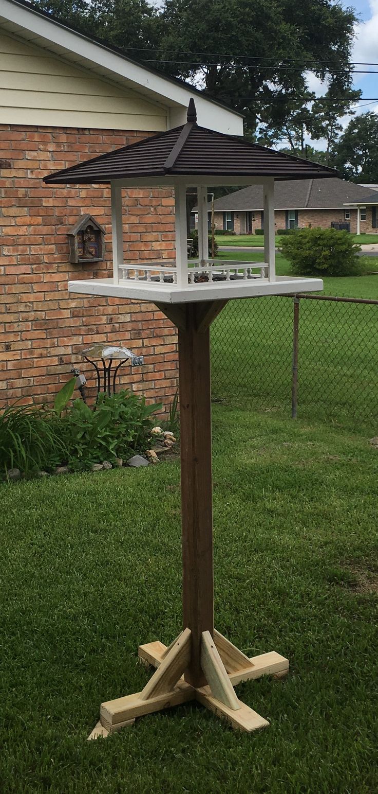 a bird feeder on top of a wooden post in the grass next to a brick building