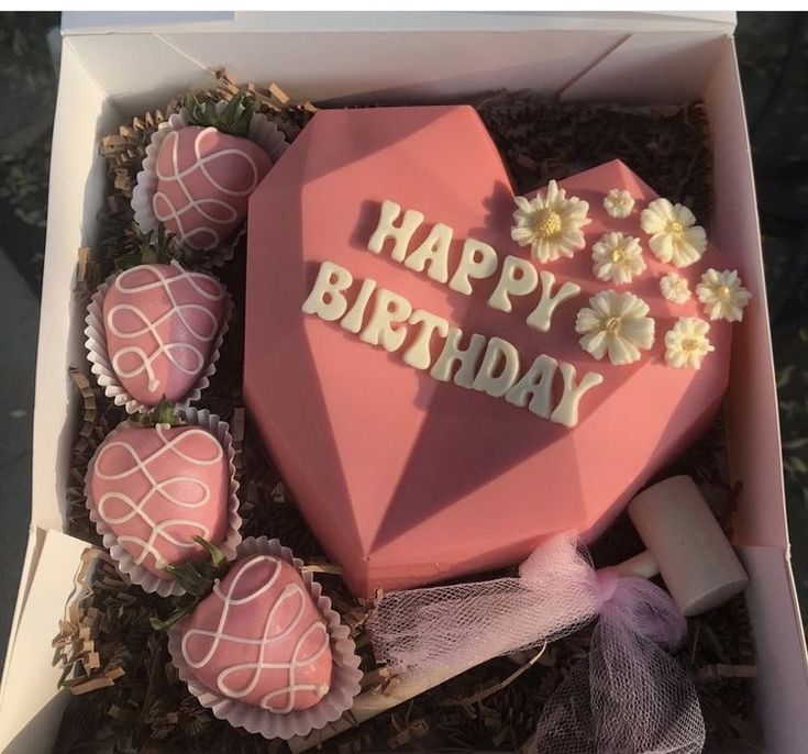 a pink heart shaped cake in a box with flowers and candles on it that says happy birthday