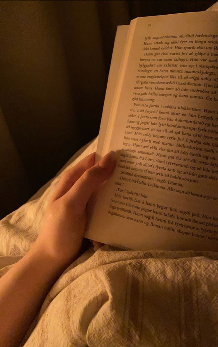 a person laying in bed reading a book with their hand on the open book's cover