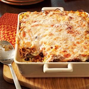 a casserole dish with meat and cheese in it on a wooden board next to a spoon