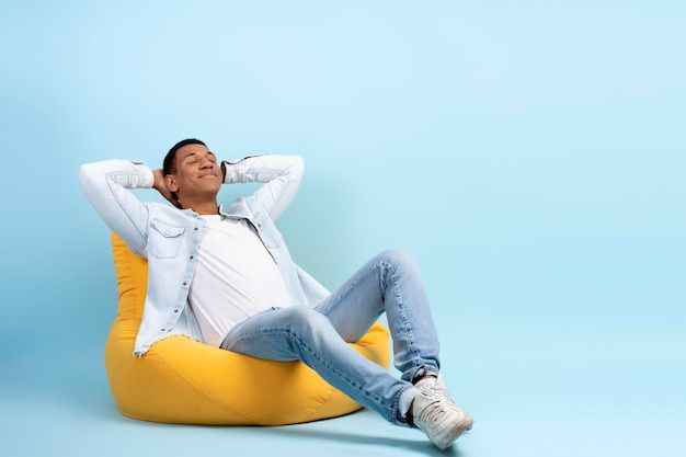 a man sitting on a bean bag chair with his hands behind his head and eyes closed