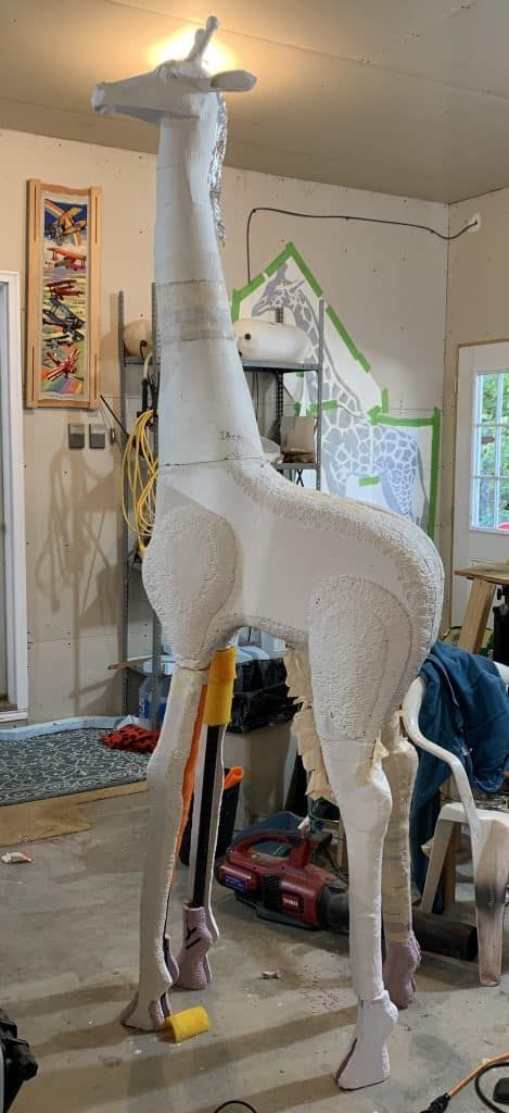 a large white giraffe standing on top of a floor next to a pile of tools