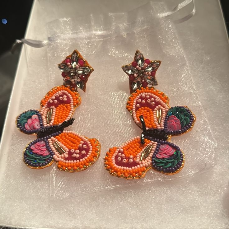 two orange and pink earrings sitting on top of a white box next to each other