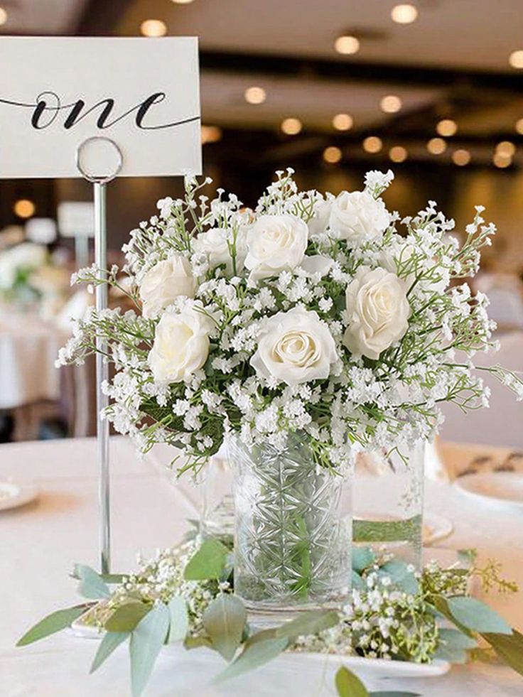 a vase filled with white flowers sitting on top of a table next to a sign