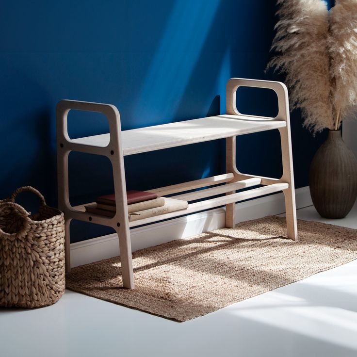 a white bench sitting next to a blue wall with a basket and vase on the floor