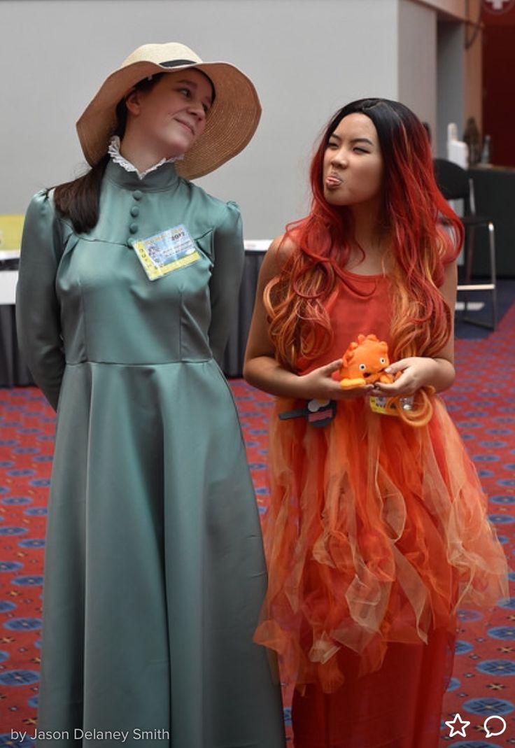 two women standing next to each other with hats on their heads and one wearing an orange dress