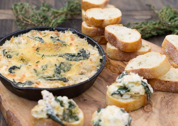 bread and spinach dip in a black bowl on a cutting board with slices of bread