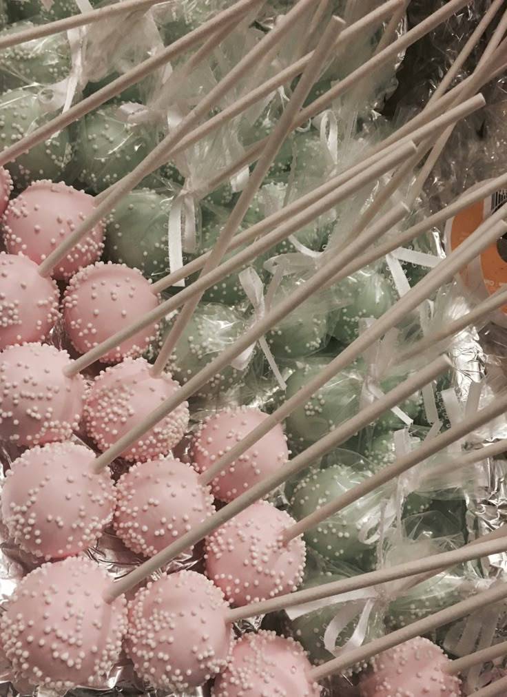 some pink and green cake pops are in plastic wrappers next to eachother