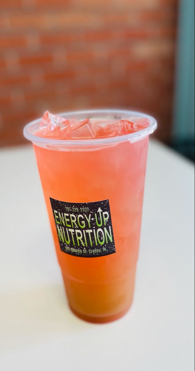 a plastic cup filled with orange liquid sitting on top of a white table next to a brick wall