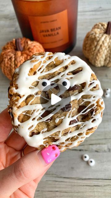 a person holding a cookie with icing and eyes on it next to some pumpkins