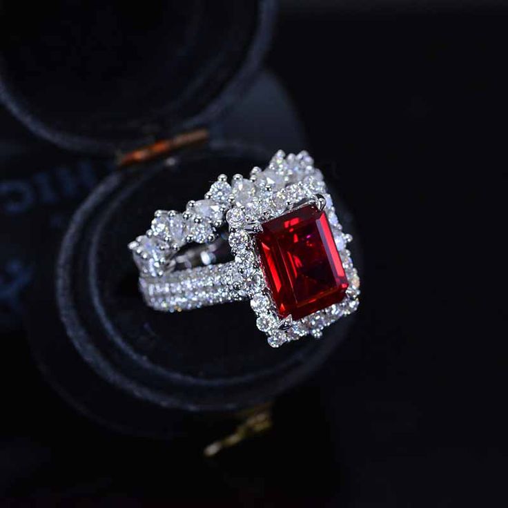 an engagement ring with a large red stone surrounded by white diamonds in a black box