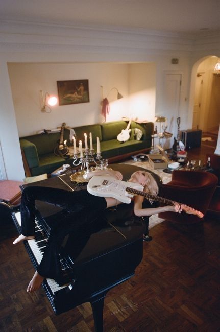 a woman laying on top of a piano in a living room next to a couch