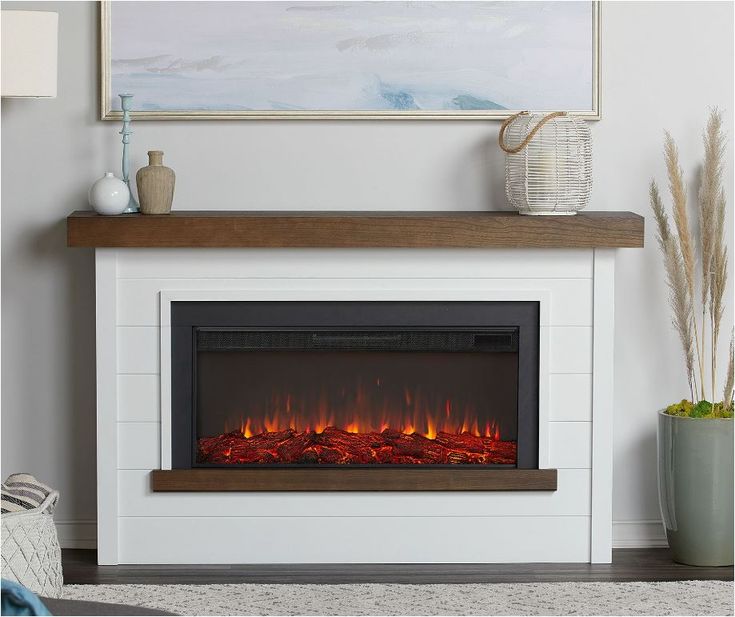 a white fireplace with red flames in the middle and a painting on the wall above it