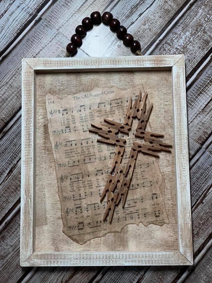 a cross made out of old sheet music is hanging on a wooden wall with beads