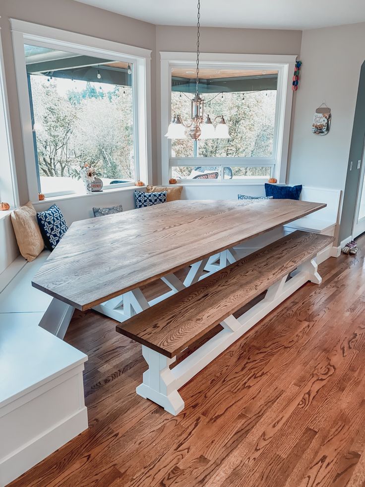 a large wooden table sitting in the middle of a room next to a window with lots of windows