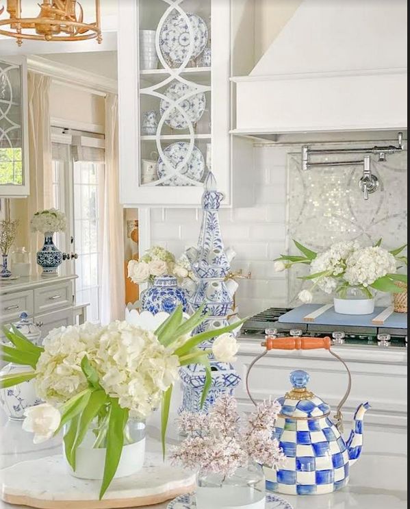 a kitchen with blue and white vases on the counter, flowers in glass teapots