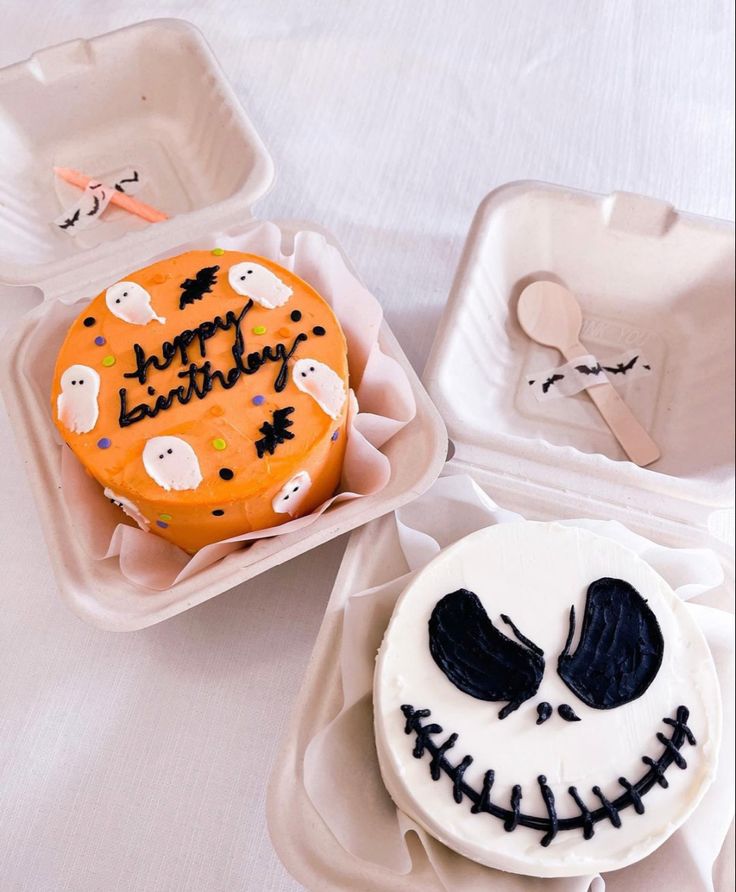 there are two halloween themed cakes in the trays on the table, one is decorated with icing and the other has spooky eyes