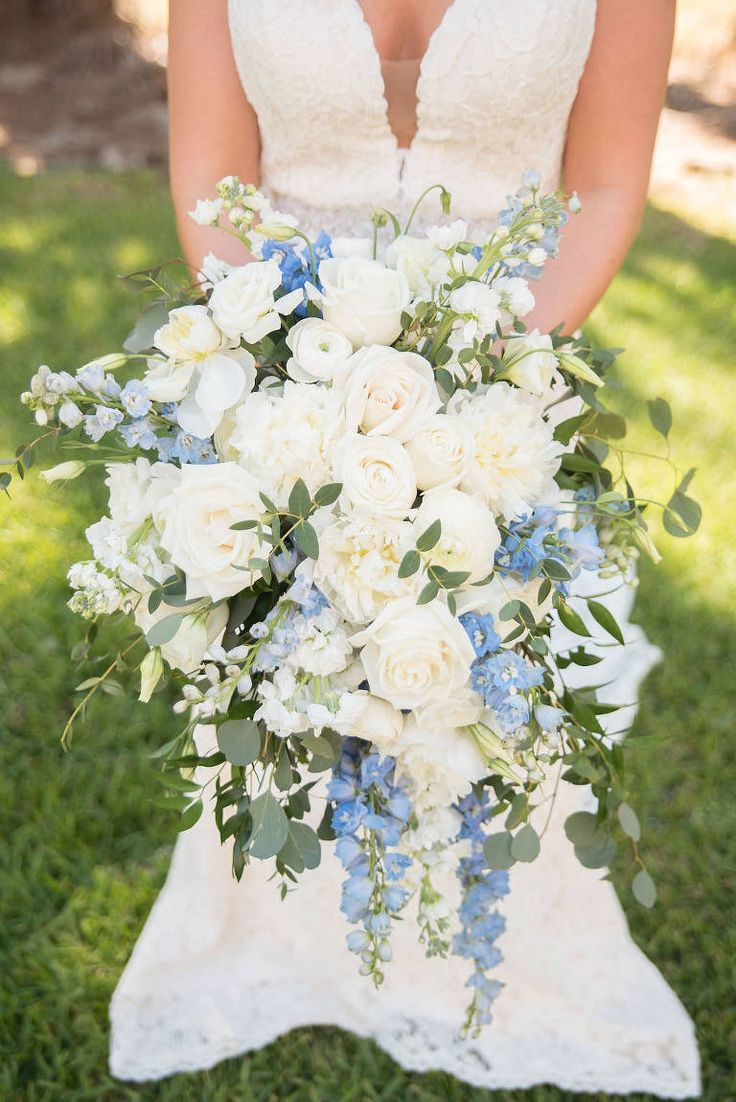 a bride holding a bouquet of white and blue flowers on her wedding day in the grass