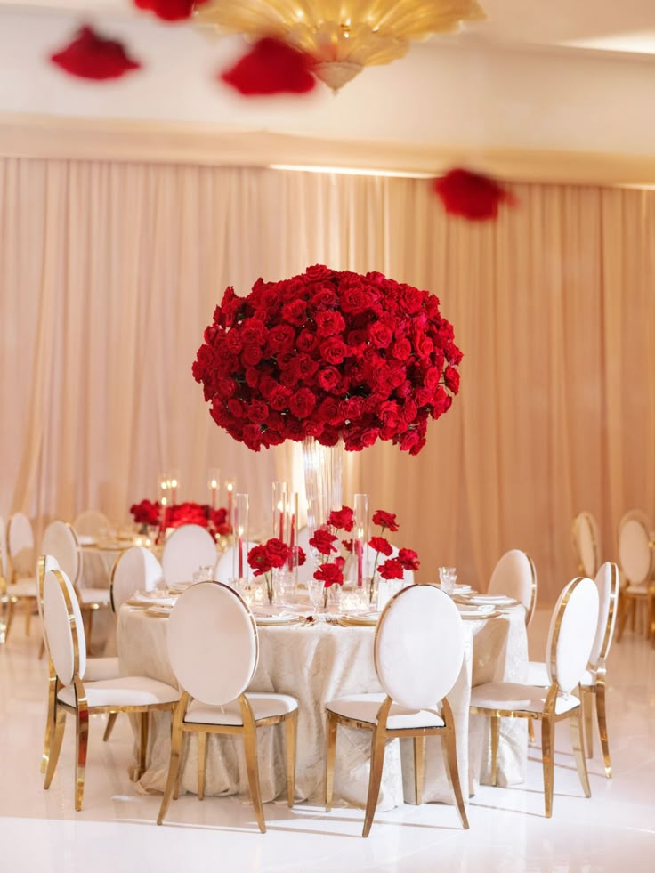 a table with white chairs and red flowers in the center is set up for a formal function