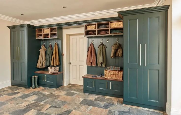 a mud room with green cabinets and coats hanging on the wall, two benches in front of them