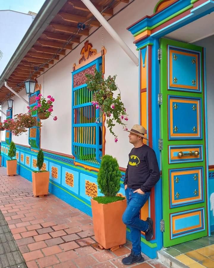 a man leaning against a colorful building with potted plants on the front and side