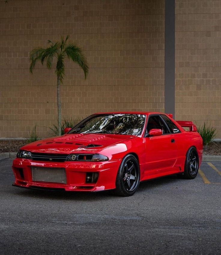 a red sports car parked in front of a brick building with palm trees behind it