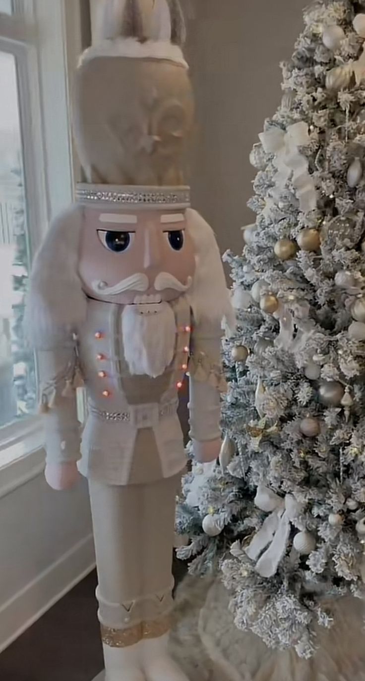 a white christmas tree in the corner of a room next to a large nutcracker