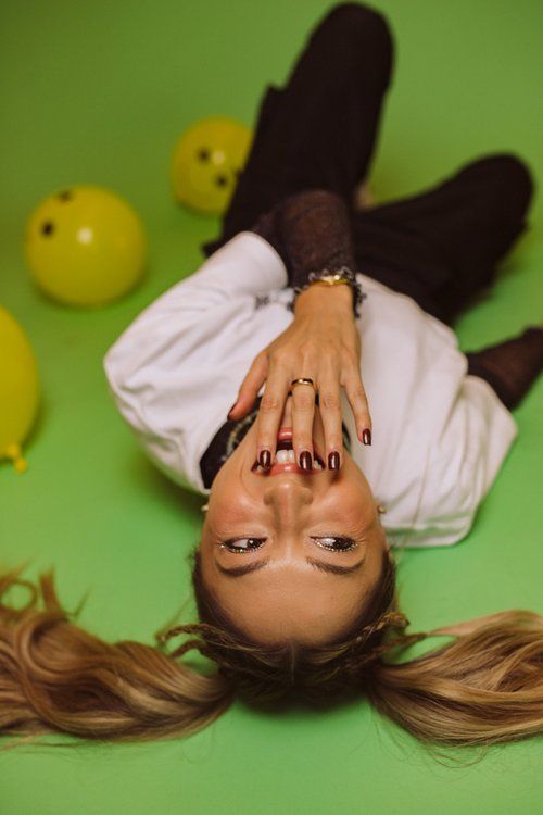 a woman laying on the ground with her hands over her head and eyes closed, surrounded by yellow balls