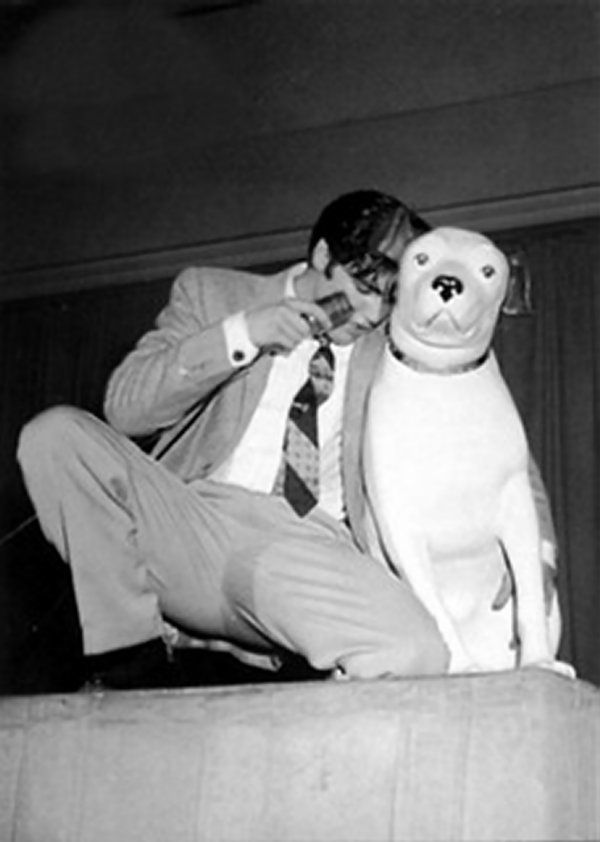 a man in a suit and tie leaning on a large stuffed dog with his mouth open