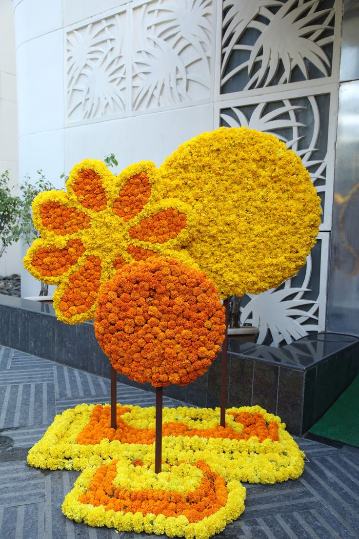 an arrangement of orange and yellow flowers on display in front of a building with white walls