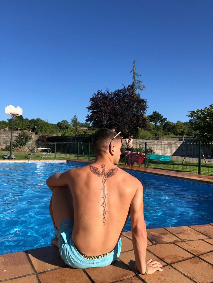 a man sitting on the edge of a swimming pool with his back to the camera