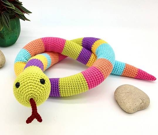 a knit snake toy sitting next to some rocks and a potted plant on a white surface