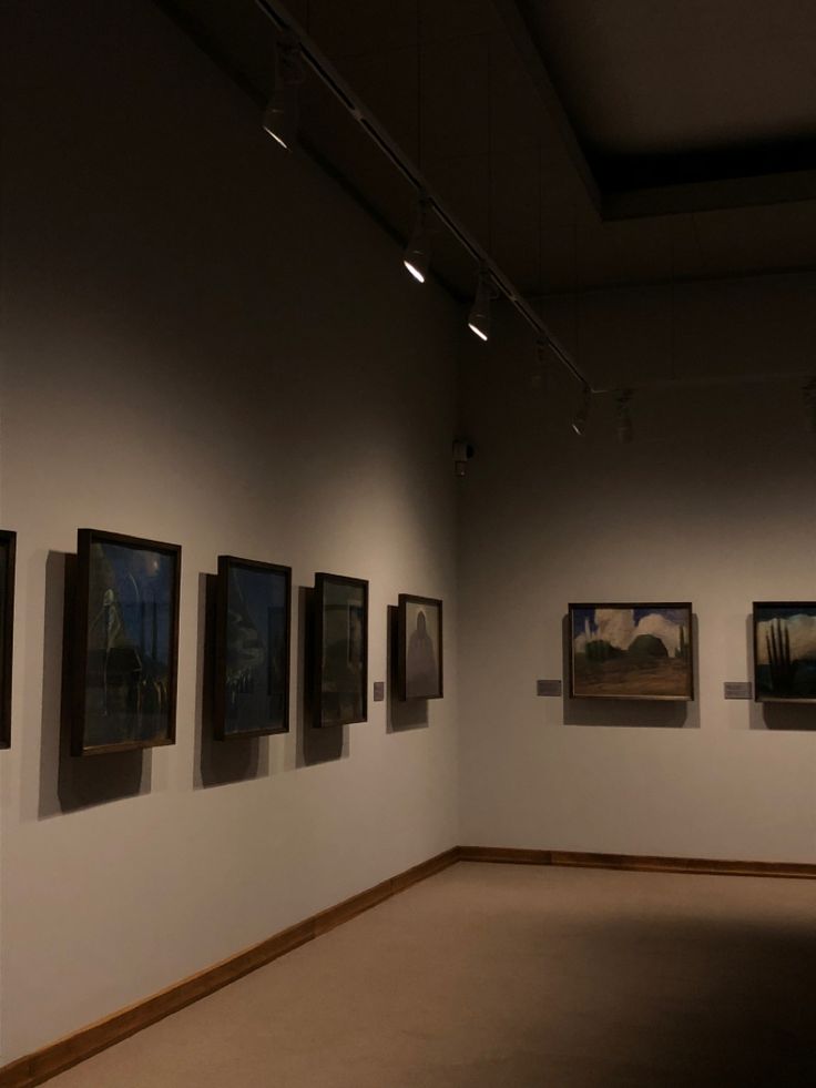 an empty room with paintings on the wall and lights hanging from the ceiling above it