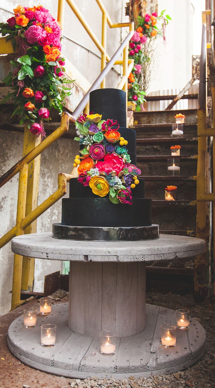 a three tiered black cake with colorful flowers on top and candles in the bottom