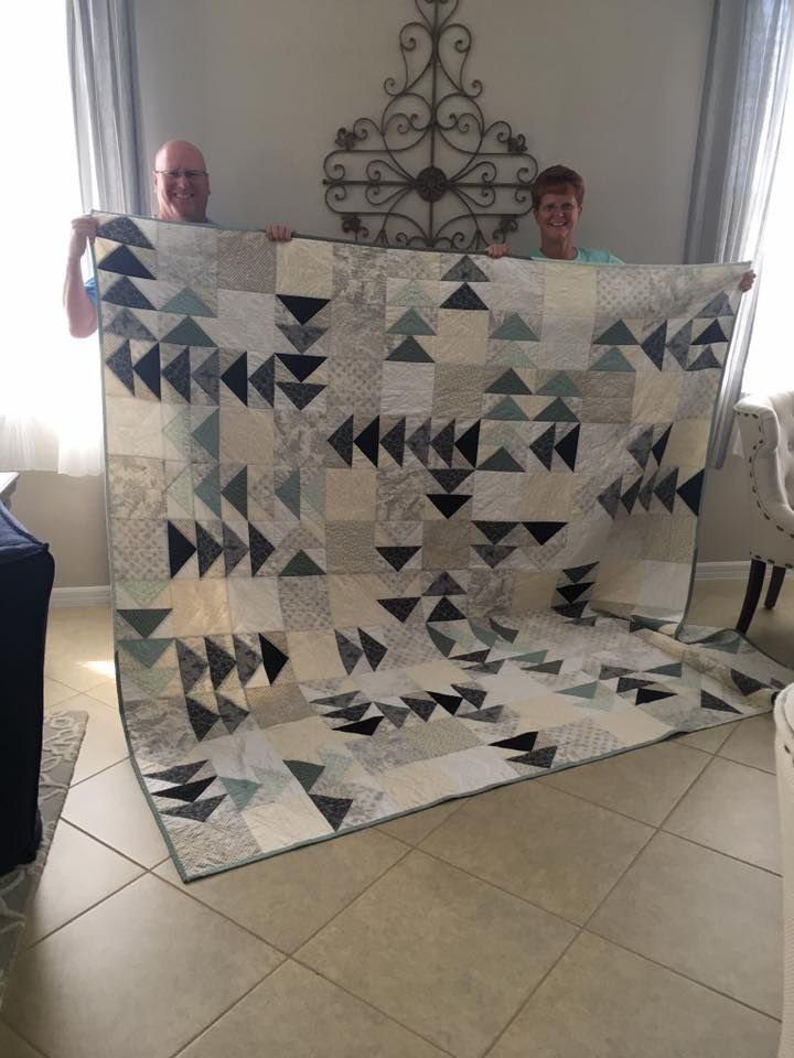 two men holding up a large quilt on the floor