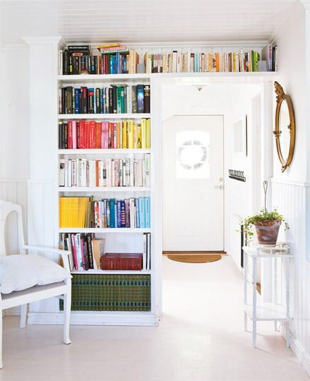 a book shelf filled with lots of books next to a white chair and table in front of a doorway