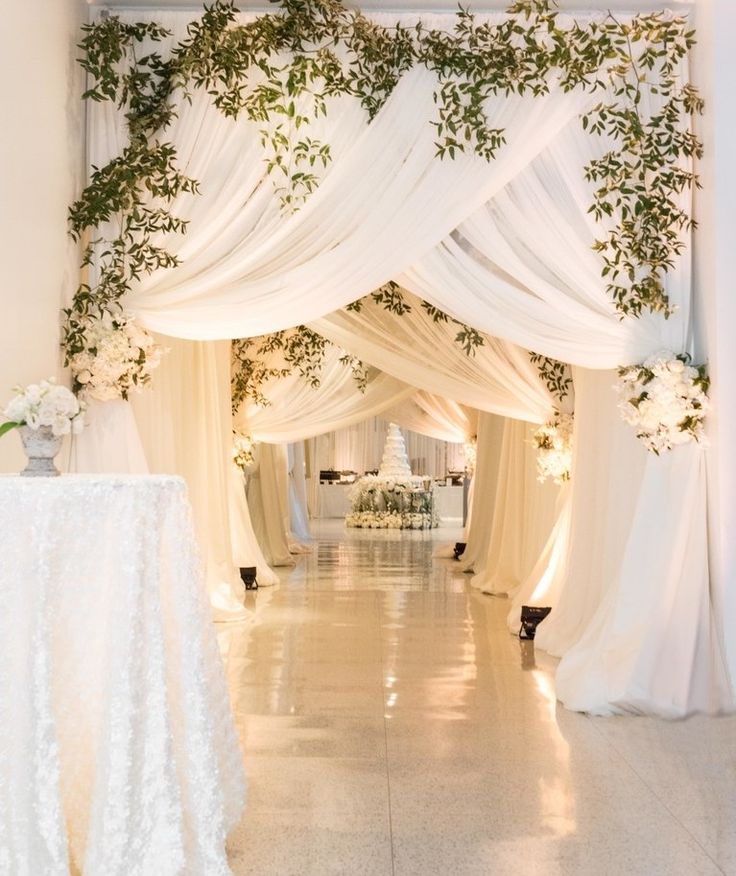 an aisle with white drapes and greenery on the ceiling, decorated with flowers