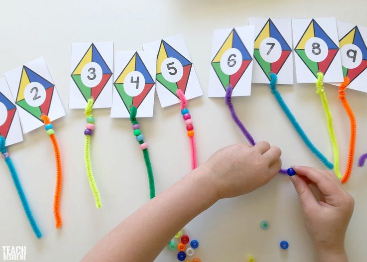 a child's hand is writing numbers on paper with colorful string and beads next to them