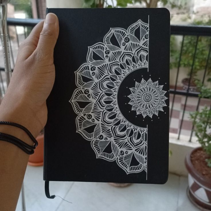 a hand holding up a notebook with an intricate design on the front and back cover