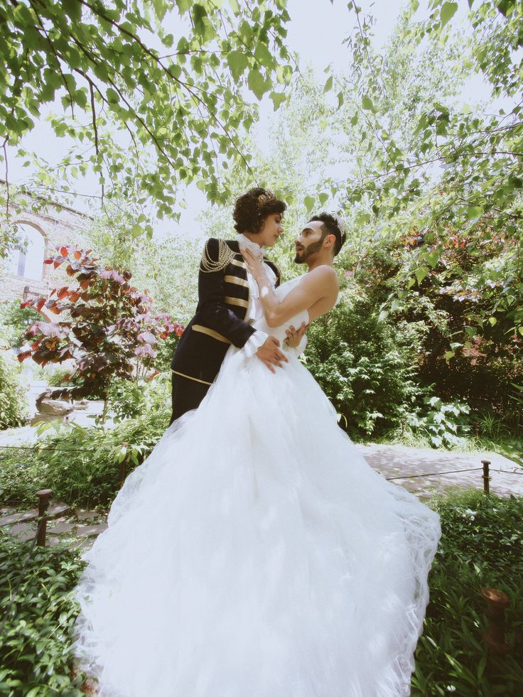 a man and woman dressed in formal wear standing under trees with their arms around each other