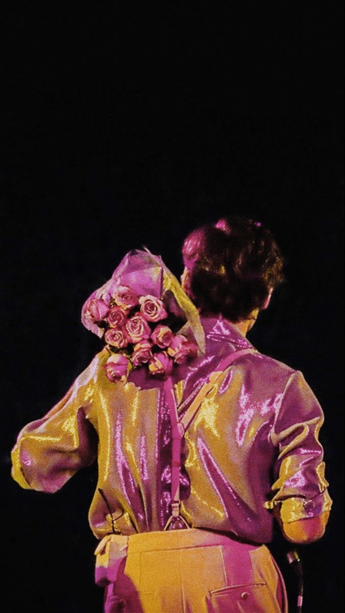 a woman with flowers on her head is standing in front of a black background wearing a gold jacket