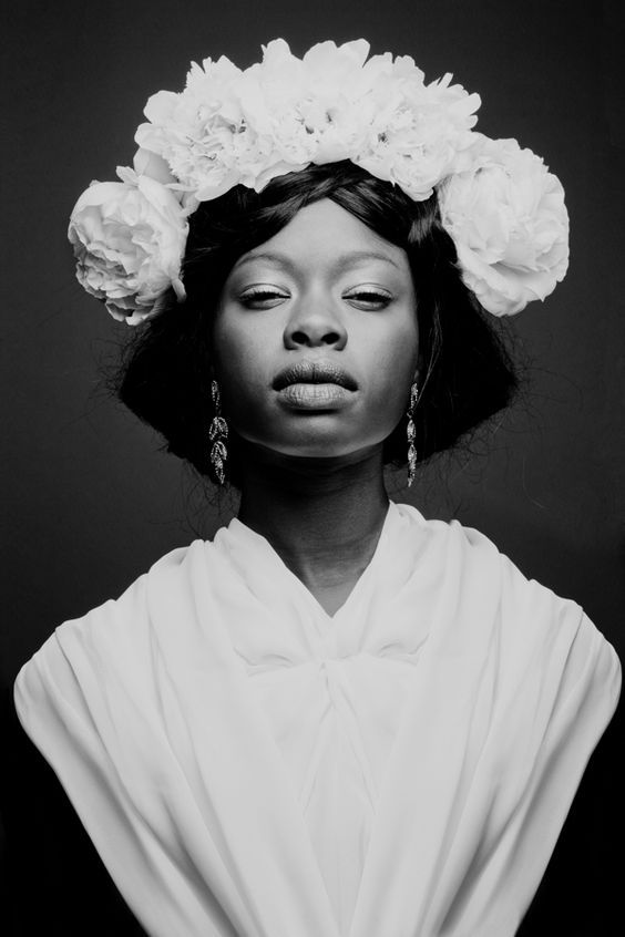 a black and white photo of a woman with flowers in her hair, wearing earrings