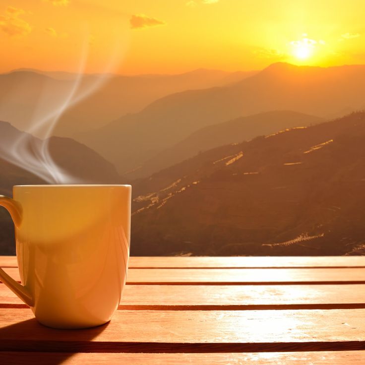 a coffee cup sitting on top of a wooden table with the sun setting in the background