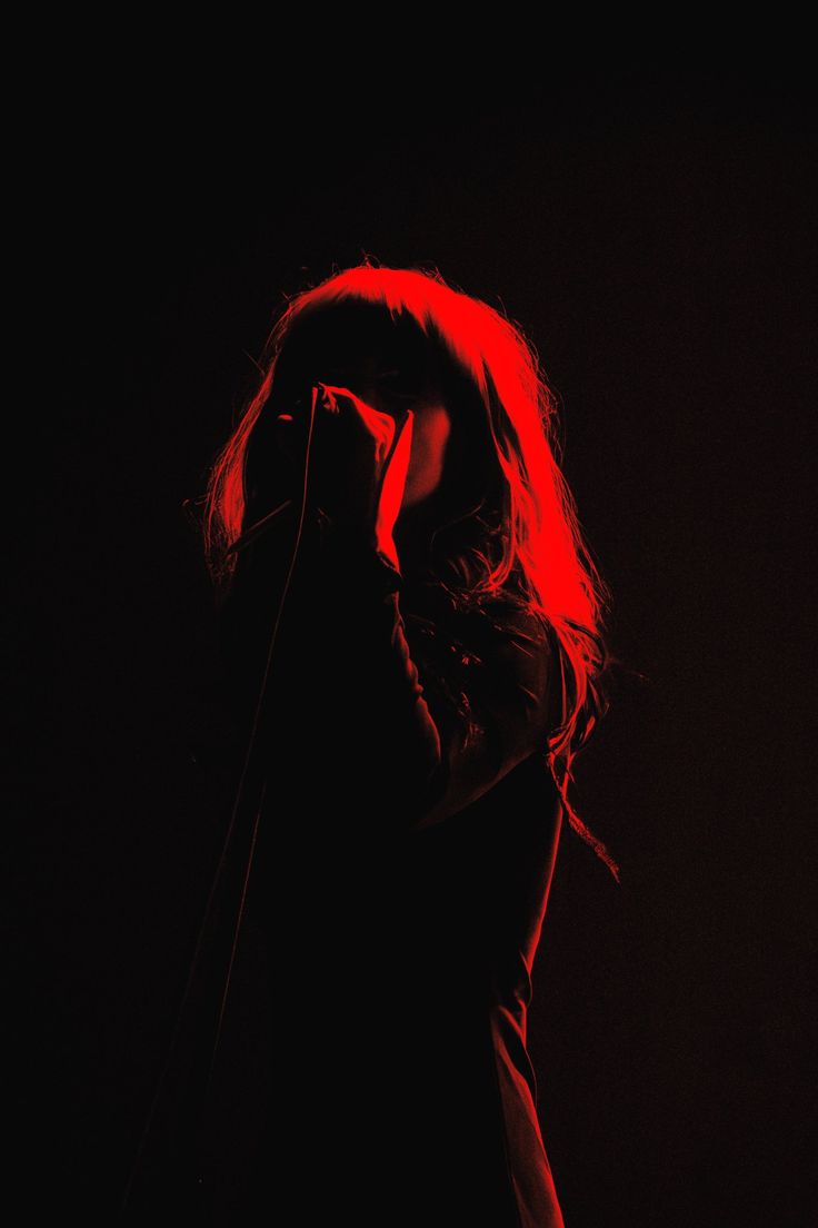 a woman standing in front of a microphone with red light on her face and long hair