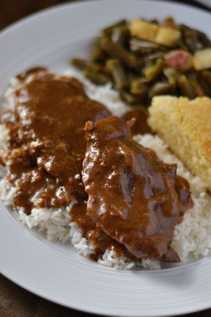 a white plate topped with rice and meat covered in gravy next to green beans