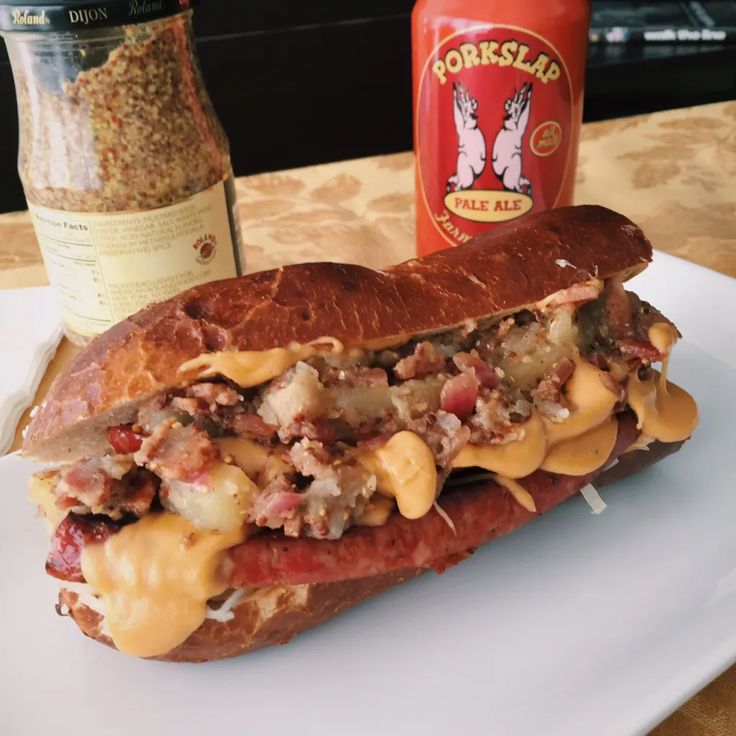 a sandwich with cheese and meat on it sitting on a plate next to a bottle of mustard