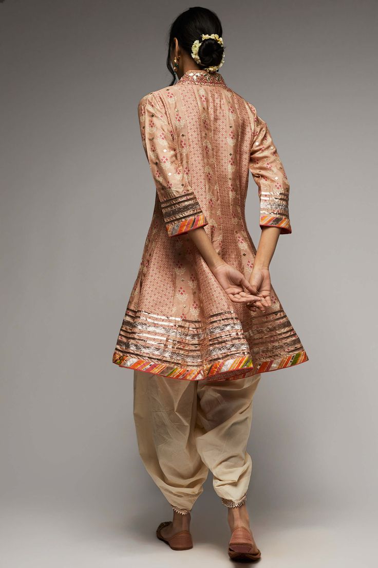 Editor's Note Indulge in the elegance of the tilla kurta and dhoti set, intricately embroidered with zardosi work and adorned with a strong floral butta and geometric jaal. Delicately enhanced with tiny motifs in silver foil, the ensemble exudes a subtle shimmer and richness. Gota motifs scattered all over accentuate the neckline, adding to its charm. Fabric: Kurta: tussar silk, dhoti: cotton Color: Pink Component: Kurta and dhoti Occasion: Festive Note: Product colour may slightly vary due to p Bollywood Style Kurta With Traditional Drape And Cutdana, Embroidered Slub Silk Sherwani With Traditional Drape, Traditional Slub Silk Sherwani For Transitional Season, Traditional Embroidered Slub Silk Sherwani, Unstitched Slub Silk Sherwani For Transitional Seasons, Bollywood Style Embroidered Slub Silk Sherwani, Festive Cotton Silk Palazzo Set With Intricate Embroidery, Transitional Unstitched Slub Silk Sherwani, Cotton Silk Sherwani With Chikankari Embroidery