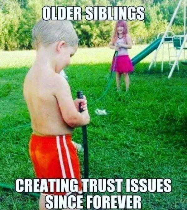 a young boy holding a water hose while standing in the grass next to another child