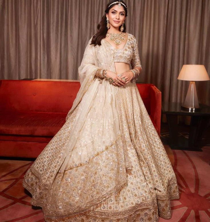 a woman in a white and gold lehenga standing on a red carpet next to a couch